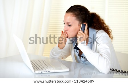 Lovely young woman kissing to laptop screen while conversing on phone