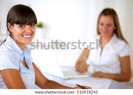 Hispanic young businesswoman looking at you at office while working on team