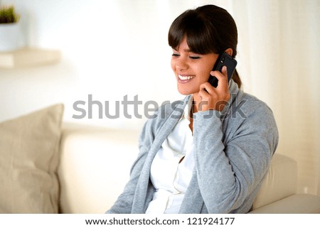 Portrait of a charming young woman conversing on mobile phone sitting on couch at home