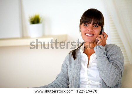Portrait of a positive smiling woman conversing on cellphone at home indoor