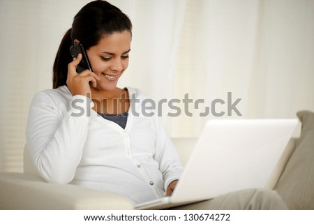 Portrait of a young woman conversing on cellphone in front of her laptop computer