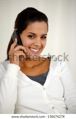 Portrait of a smiling young woman speaking on cellphone while is looking at you