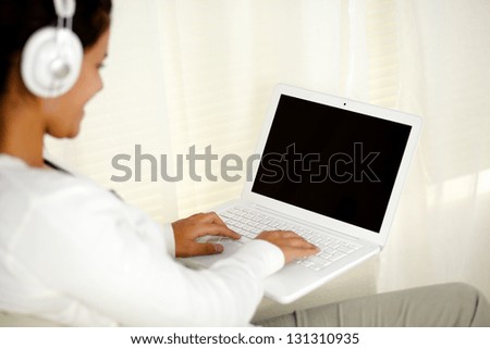 Portrait of a young woman working on laptop while is listening music with headphone
