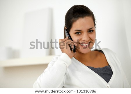 Portrait of a charming young woman conversing on mobile phone while is looking at you