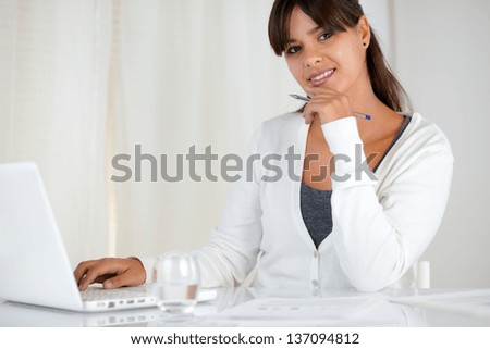 Portrait of a smiling young woman looking at you using her laptop at office - copyspace