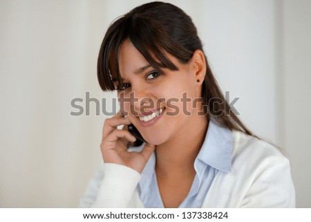 Portrait of a smiling young woman looking at you while is speaking on cellphone at soft colors composition
