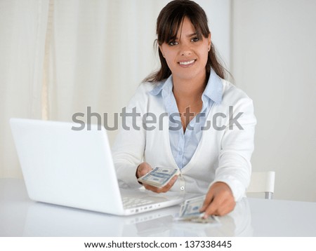 Portrait of a young woman counting cash money for buying while is looking at you in front of her laptop computer