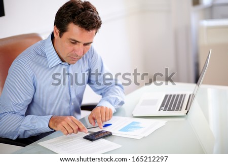 Portrait of a hispanic employee on blue shirt working with his calculator while sitting on office desk