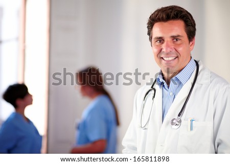 Portrait of an adult hispanic doctor on white coat standing and smiling on medical women team background