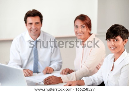 Portrait of charming latin group smiling and looking at you while sitting on office desk