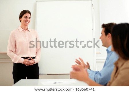 Portrait of professional team giving applause to a pretty businesswoman with pink shirt who is standing in front of whiteboard at end of conference