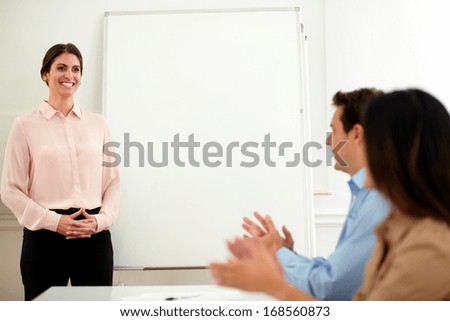 Portrait of professional team giving applause to businesswoman with pink shirt who is standing in front of whiteboard at end of conference