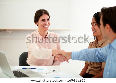 Portrait of charming young lady on pink blouse giving greeting gesture to handsome businessman on office desk