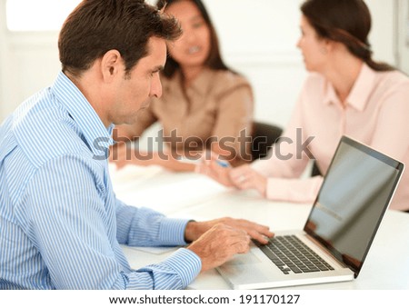 Portrait of attractive man working on his laptop while sitting with two office coworker in background