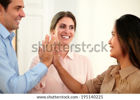 Portrait of adult businesswoman on pink blouse huddle her hands with her coworkers while smiling at asiatic girl and standing on office background
