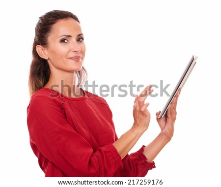 Portrait charming hispanic woman on red shirt using her tablet pc while smiling at you on isolated studio