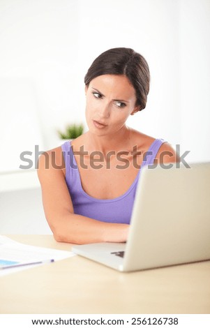 Young angry woman in purple t-shirt working on the computer in her house