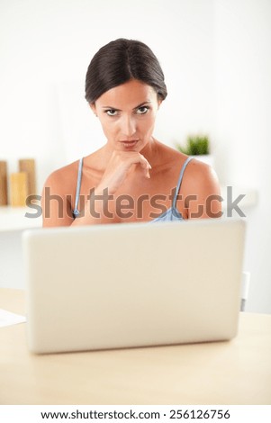 Stylish woman in blue blouse sitting while studying on her laptop and looking angry at indoor