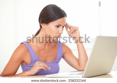 Fatigued lady in purple shirt surfing the web on her computer while sitting indoor