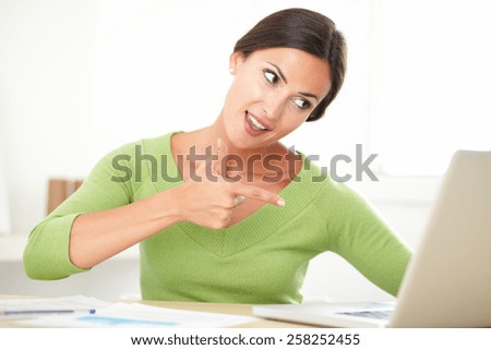 Cheerful young lady in green shirt looking excited over a success while surfing the web indoor