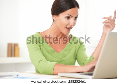 Elegant young woman celebrating over a success while browsing the web on the computer at home