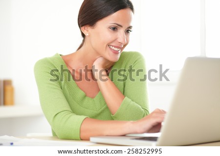 Pretty latin lady in green shirt smiling while working on her laptop at home