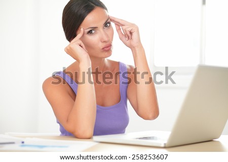 Attractive hispanic lady with headache using her laptop in the house desk