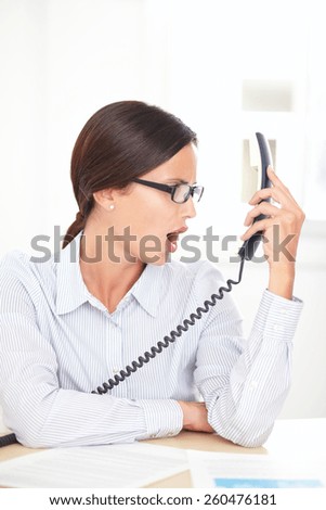 Latin professional employee with spectacles screaming on the phone at her workplace