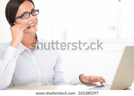Charming callcenter employee with glasses working on the desk while smiling and looking at you
