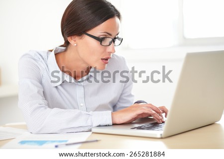 Latin pretty receptionist with spectacles working on the laptop while looking shocked
