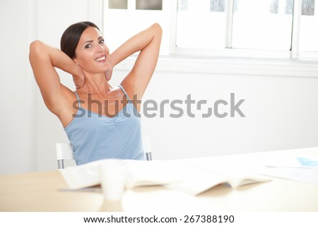 Smart woman in blue blouse looking satisfied and relaxed while studying a book in her room