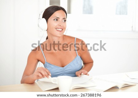 Pretty woman in blue shirt with headphones listening to music and looking happy to her left - copyspace