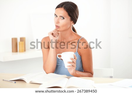 Adult beautiful woman in blue shirt wondering while studying her books at her house