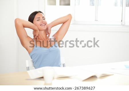 Cheerful adult woman in stylish blouse sitting on her desk and looking relaxed