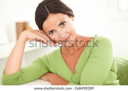 Young beautiful woman with hand on face looking at the camera while smiling with confidence at home