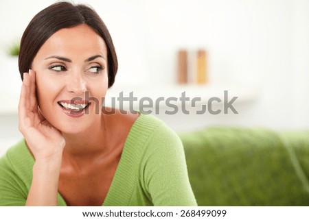 Beautiful woman with brown hair smiling and looking away while putting hand on face - copy space