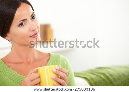 Contemplative woman with brown hair sitting in the house and holding a yellow mug - copy space