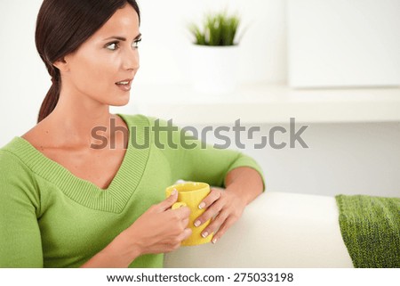Peaceful woman in a green shirt holding a yellow mug while looking away - focus on foreground