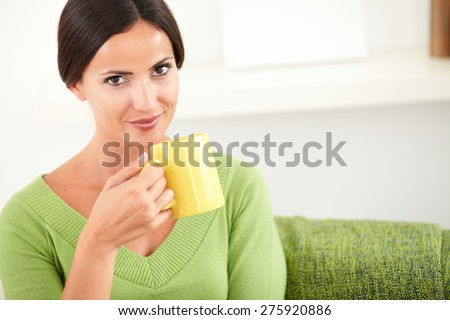 Attractive lady in green shirt holding a yellow mug while looking at the camera - copy space