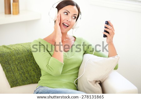 Waist up portrait of a young female enjoying music on headphones while sitting indoors