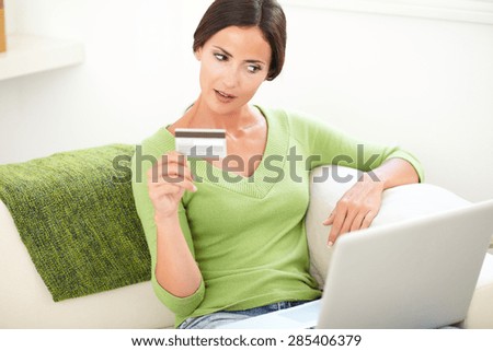 Young woman in green shirt holding a credit card while looking at her laptop