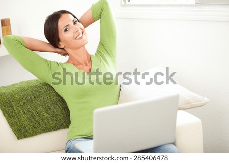 Calm woman relaxing with her hands behind her head while holding a laptop