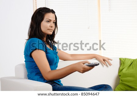 Portrait  of a beautiful young woman  changing channel with the  TV remote.
