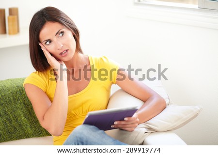 Surprised lady in yellow tank top holding a tablet while looking away from the camera - copy space