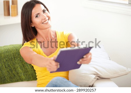 Relaxed woman of caucasian ethnicity giving you a tablet while sitting inside the house