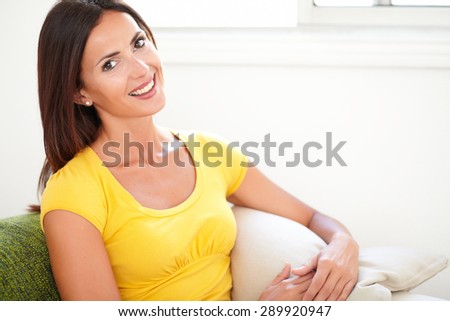 Young woman of caucasian ethnicity toothy smiling at the camera while sitting at home