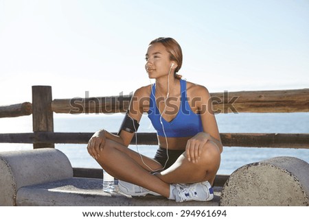 Fitness woman resting on the coastline while listening to music