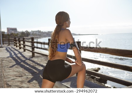 Side view of a young athlete stretching on the beach shore in summertime
