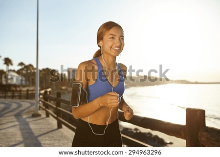Happy runner woman in blue tank top jogging on the beach while smiling