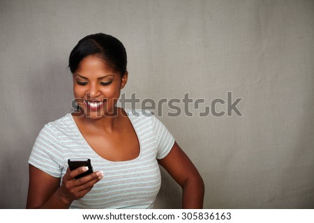 Smiling girl in grey blouse texting on her cell phone while standing - copy space